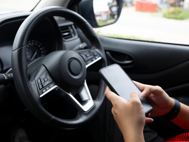 Persona enviando mensajes de texto mientras conduce con notificaciones de redes sociales, lo que simboliza la conducción distraída y el riesgo de adicción a los teléfonos inteligentes.