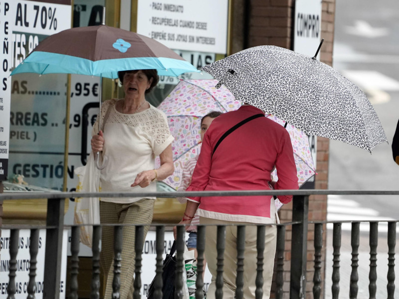 tres personas se protegen con paraguas de la lluvia que cae en el centro de Oviedo