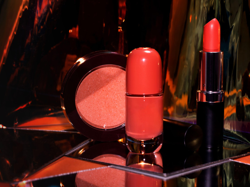 Lápiz labial rojo abierto, esmalte de uñas y rubor con reflejo de espejo sobre la superficie del vidrio.