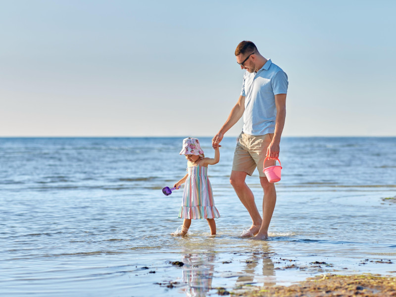Un padre camina feliz por la orilla de la playa con su hija