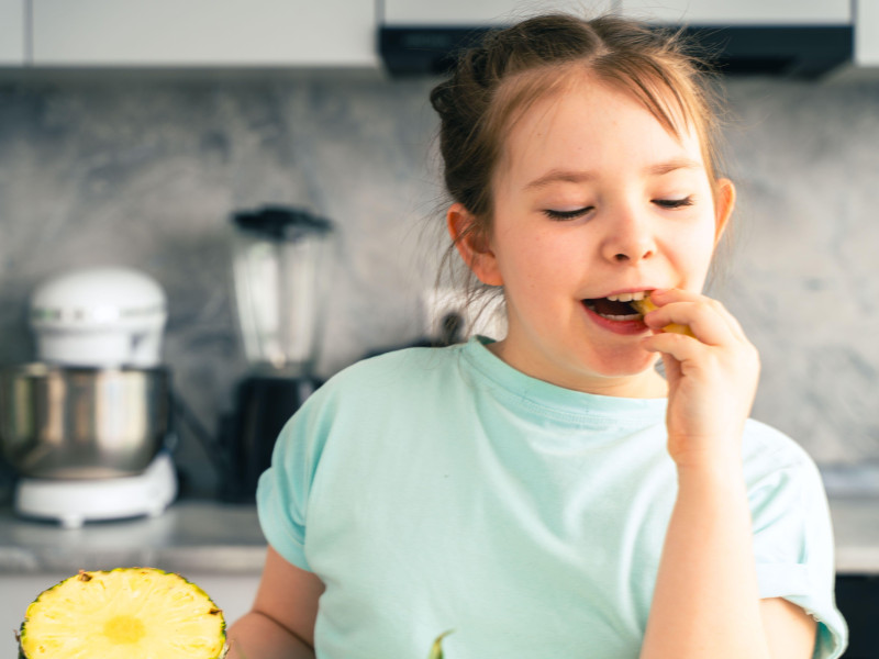 Una niña come piña mientras cierra los ojos con placer