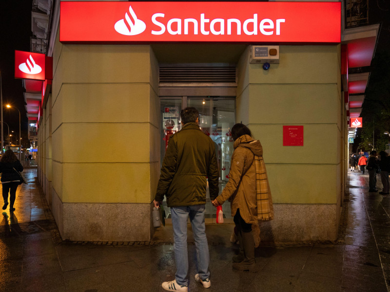Los peatones pasan junto a la sucursal del banco comercial multinacional español y de servicios financieros Santander durante la noche.