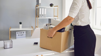 Una mujer en medio de un despido con una caja de cartón sale del lugar de trabajo desde la oficina de la empresa.