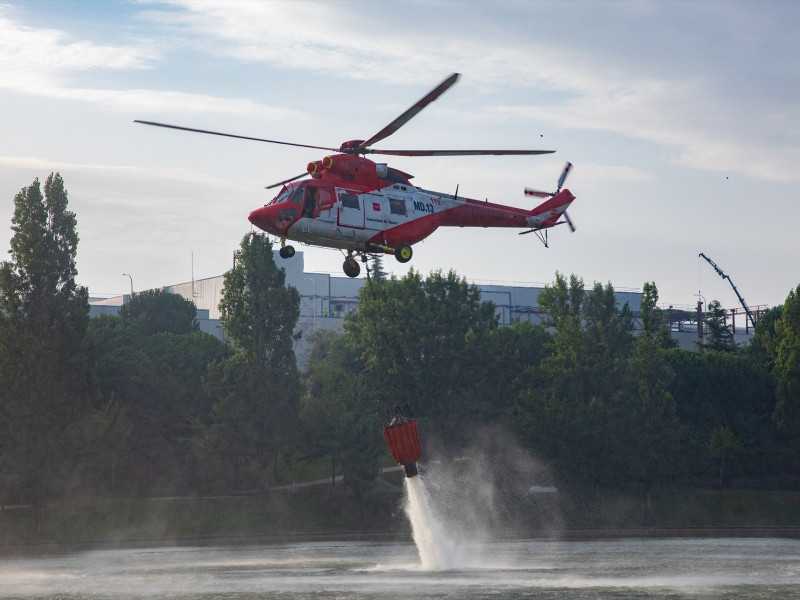 Un helicóptero recoge agua de un estanque cercano al incendio en Tres Cantos, Madrid