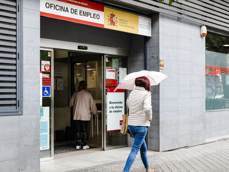 Una mujer con paraguas pasa por la oficina del paro