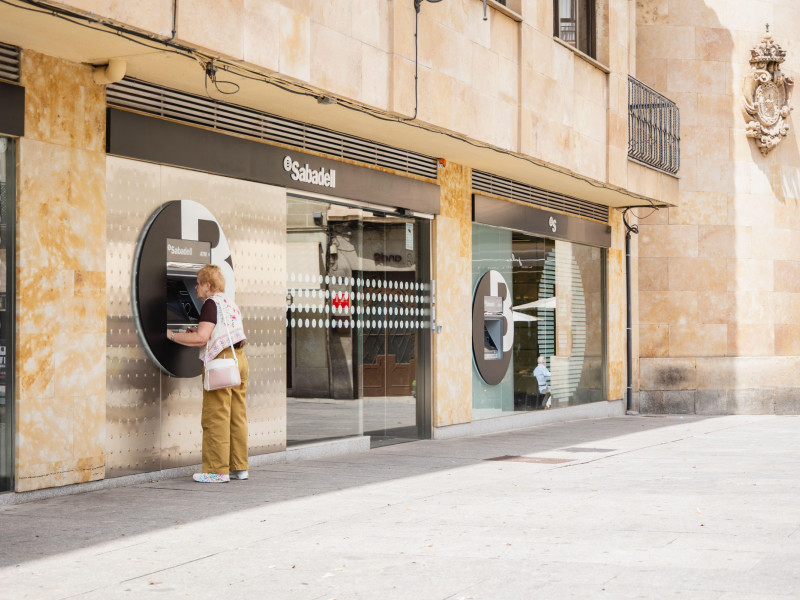 Una jubilada utiliza un cajero automático exterior del Banco Sabadell en una mañana soleada en Salamanca