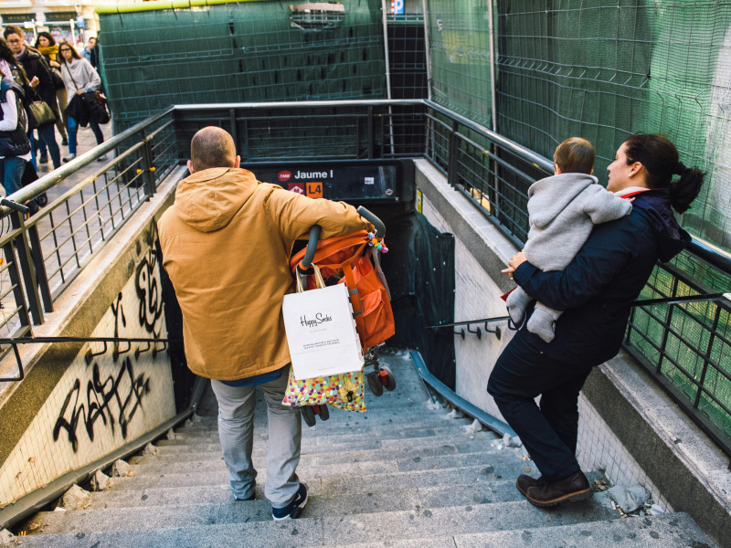 Pareja joven con niños pequeños bajando las escaleras del metro de Barcelona con el padre llevando el cochecito y la madre el bebé
