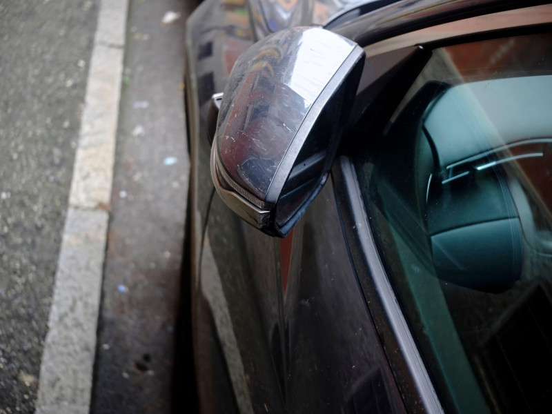 Espejo retrovisor lateral sucio que refleja un edificio, lo que resalta la necesidad de mantenimiento del automóvil.