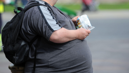 Una persona obesa comiendo un snack en la calle