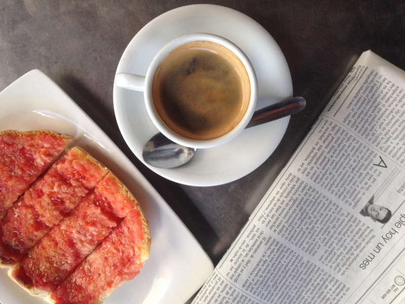 Tostada de tomate fresco y café negro en la mesa del desayuno con un periódico