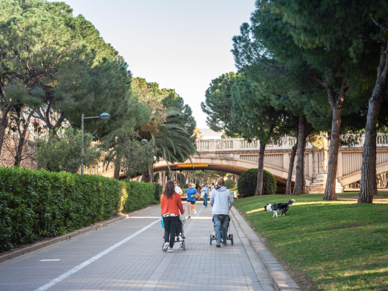 Padres jóvenes empujan cochecitos por el sendero arbolado del Jardín del Turia de Valencia