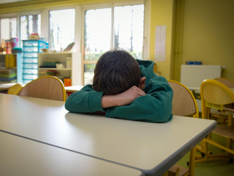Un joven niño víctima del bullying pone su cabeza y sus brazos sobre la mesa