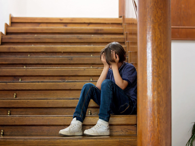 Niño triste, sentado en una escalera en una casa grande por acoso escolar