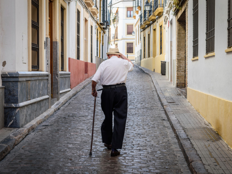 Jubilado con bastón caminando por una calle adoquinada en Sevilla, Andalucía, España.