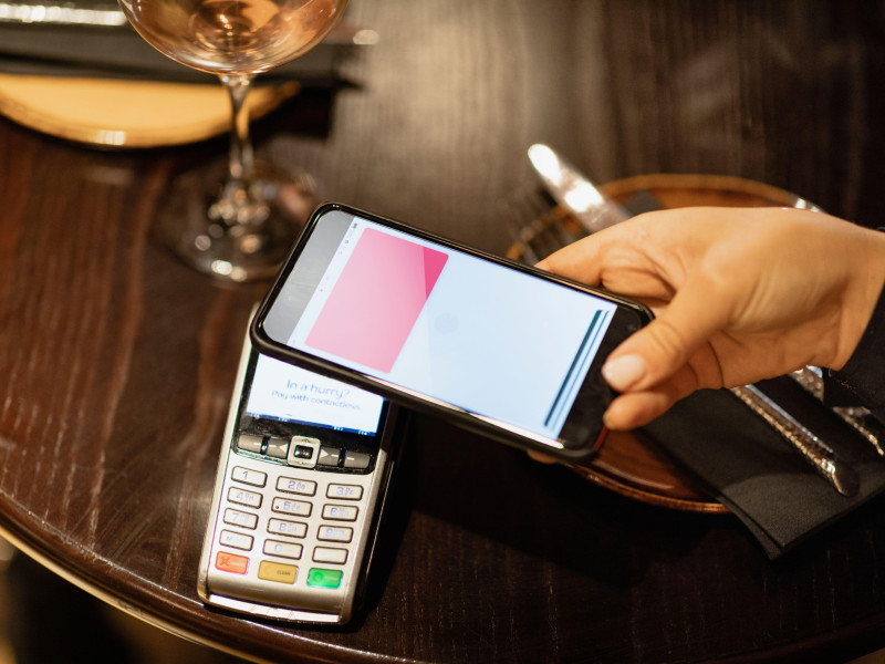 Una persona irreconocible que usa un teléfono móvil para pagar una comida.