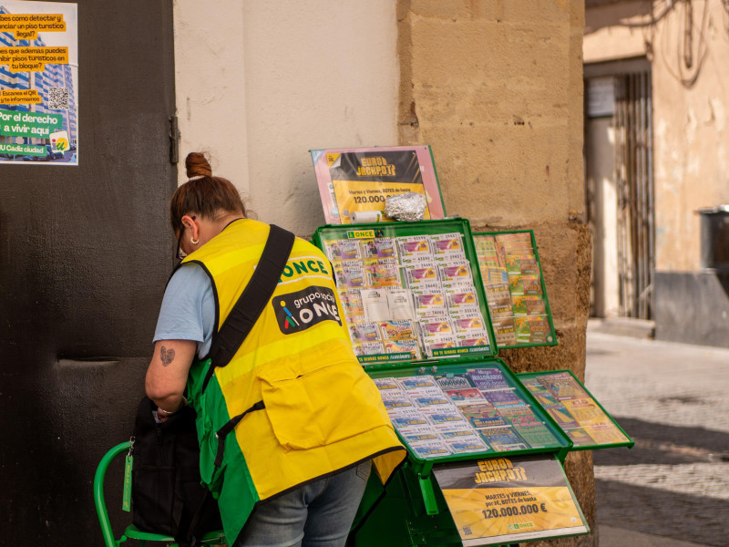 Una vendedora de lotería de la organización benéfica española Once se encuentra debajo de un cartel que aconseja a los residentes de Cádiz cómo denunciar los alojamientos turísticos ilegales.