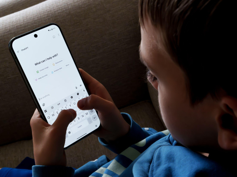 Interfaz ChatGPT utilizada por un niño pequeño en un teléfono inteligente mientras está sentado en el sofá.