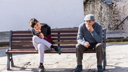 Un joven juega con su teléfono móvil sentado junto a un hombre mayor en el pueblo de Capileira, La Alpujarra, Granada