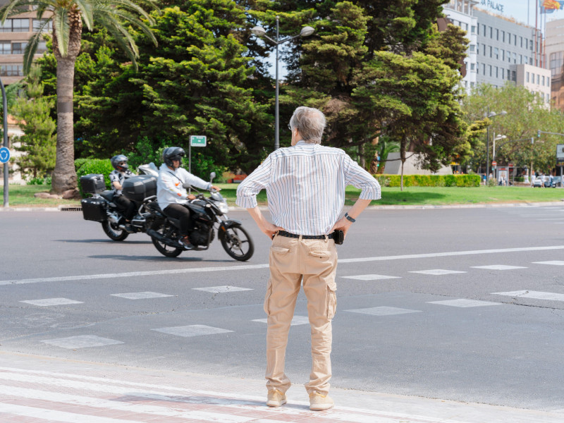 Un jubilado se encuentra en un cruce peatonal mientras dos motos pasan por una carretera de varios carriles en el centro de Valencia.