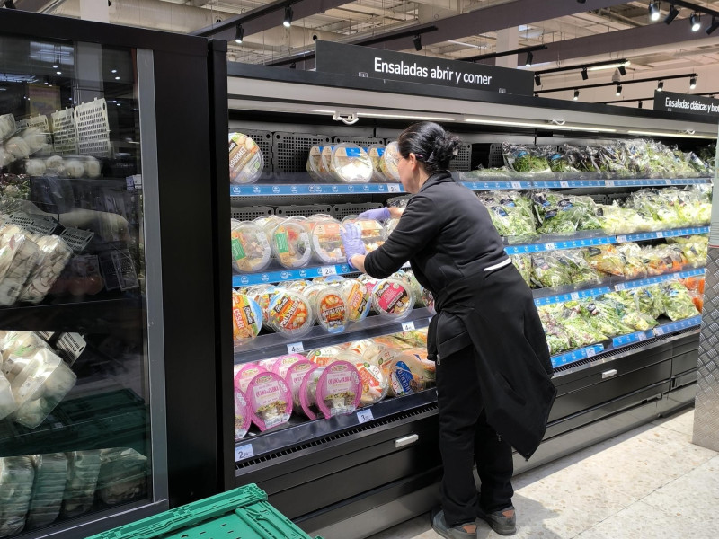 Una reponedora coloca ensaladas para llevar en las estanterías de las cámaras frigoríficas de un supermercado