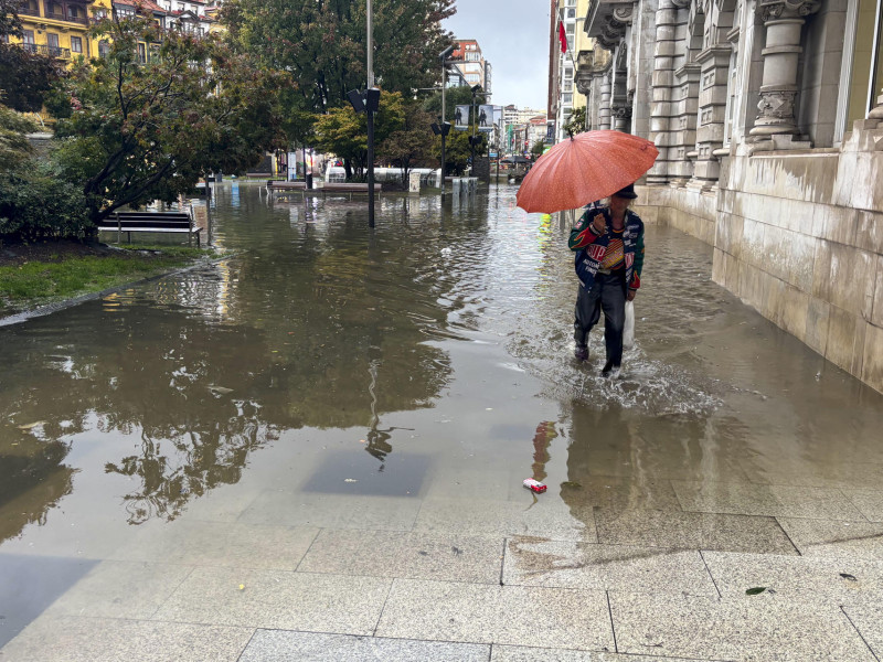 Una persona intenta atravesar una calle inundada de Santander durante la tormenta registrada