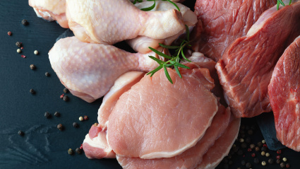 Varios tipos de carne fresca: cerdo, ternera y pollo sobre una mesa negra.