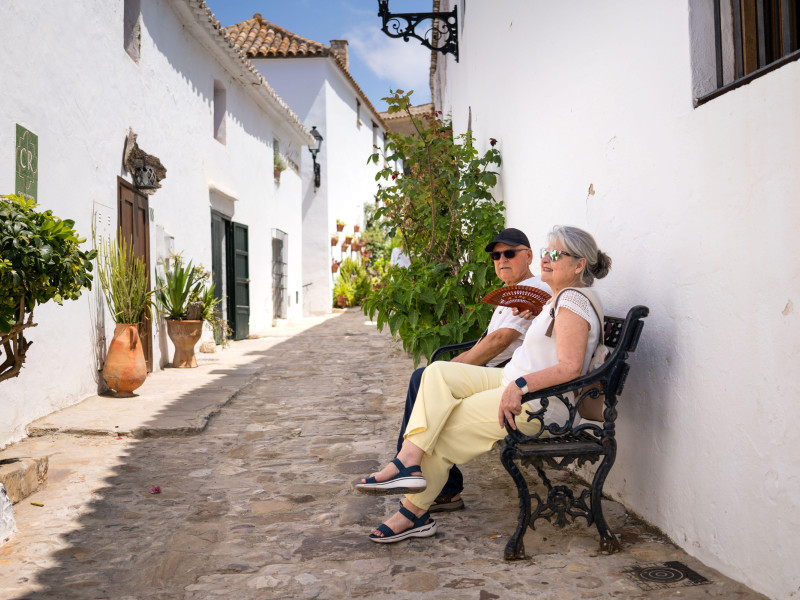 Una pareja de jubilados disfruta de un tranquilo paseo por un histórico pueblo blanco del sur de España, disfrutando del encanto y la tranquilidad de sus vacaciones.