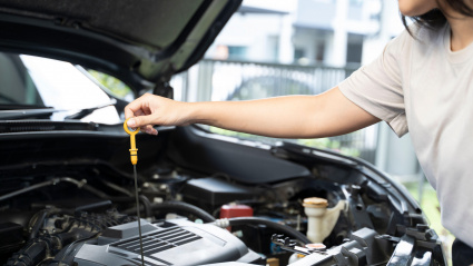 Mujer parada junto a un coche con el capó levantado, revisando el motor.
