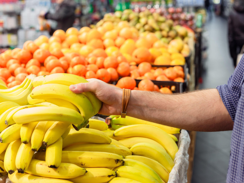 La mano del hombre toma plátanos del estante del supermercado