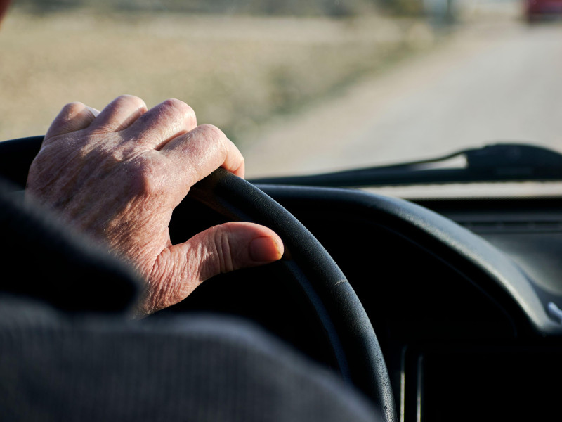 Manos de un jubilado sosteniendo el volante de un vehículo