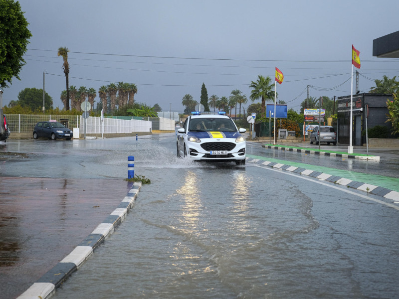 Un coche de policía circula por una calle anegada por la lluvia en Foia, en Elche