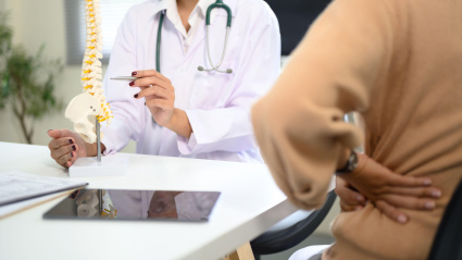 Médico explicando la anatomía de la columna con un modelo a un paciente que sufre de dolor de espalda.