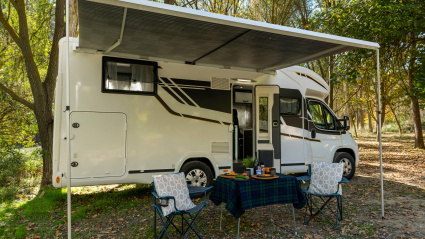 Autocaravana en camping con mesa y sillas instaladas en el exterior del vehículo y preparadas para comer y beber.