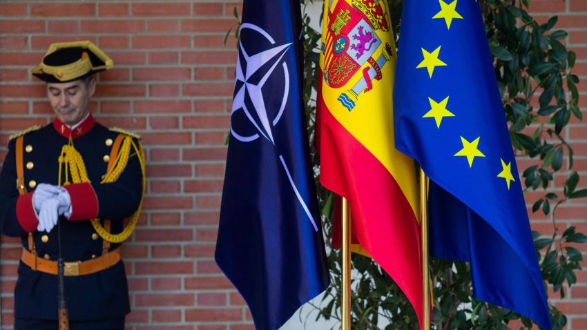 Un oficial de protocolo mira su reloj frente a las banderas de la OTAN, España y la Unión Europea.