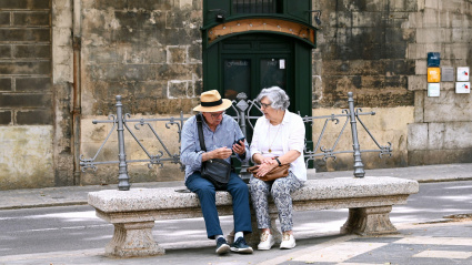 Una pareja de jubilados en un banco de piedra mirando sus teléfonos móviles, Palma de Mallorca
