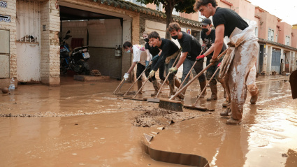 Grupo de voluntarios barre el lodo y el agua sucia de las calles hacia las alcantarillas durante las inundaciones de la dana. Alfafar