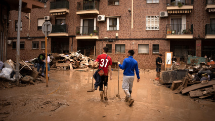 Dos jóvenes caminan por una calle embarrada e inundada en Paiporta.