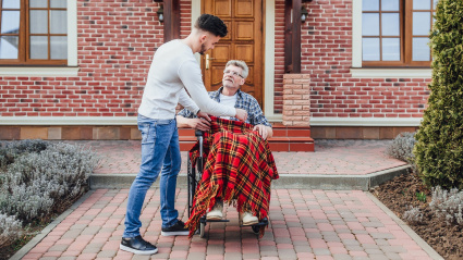 Una imagen de una persona arropando a otra que se desplaza en silla de ruedas