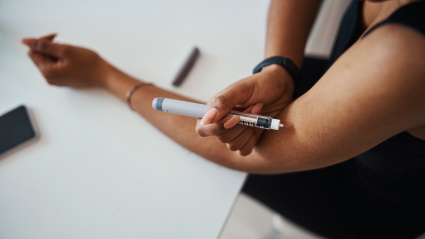 Close up of female person sitting at the table and making injection in her arm