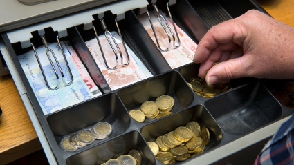 Un cajero muestra el dinero en euros de su caja registradora