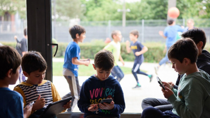 Dos grups d'infants, un jugant al patí i els altres davant les pantalles