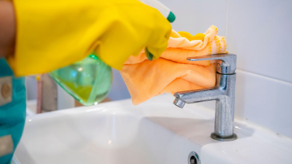 Empleada del hogar limpiando el grifo de un baño