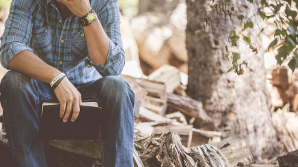 Un hombre sujeta un libro, sentado entre la naturaleza