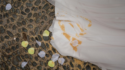 Un vestido de novia yace sobre un camino empedrado, manchado de tierra y rodeado de pétalos de flores esparcidos.