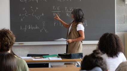 Profesora dando una clase de ciencias, explicando en la pizarra.