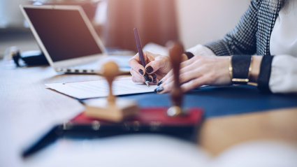 Una mujer escribe en en una mesa con varios objetos de escritorio