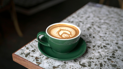 Taza de café Flat White en una taza verde con un hermoso arte latte, sobre una mesa de mármol.