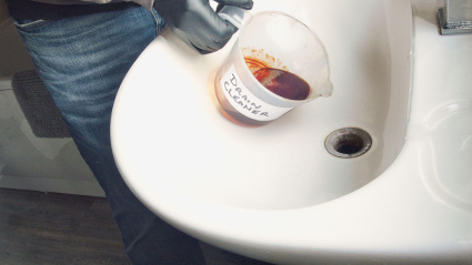 Las manos de un fontanero con guantes de goma negros vierten limpiador de desagües en el desagüe del lavabo para destaparlo.