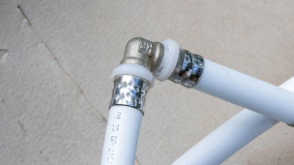 Los tubos de plástico blanco están conectados con un conector de esquina de metal, lo que muestra el trabajo de plomería en progreso.