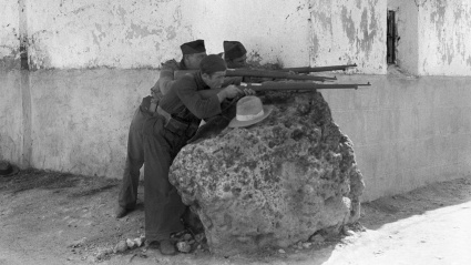 Combatientes republicanos protegidos tras una roca natural abren fuego de fusil sobre el enemigo durante la Guerra Civil